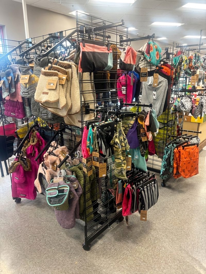 A rack of dog coats, sweaters, vests and bandanas